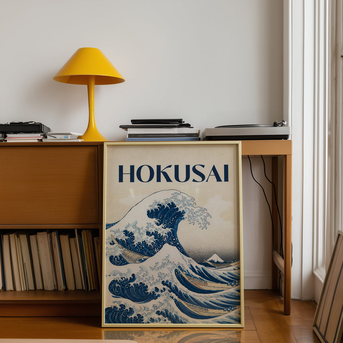 Great Wave with HOKUSAI title print shown in a gold frame leaning under a teak desk with a yellow lamp