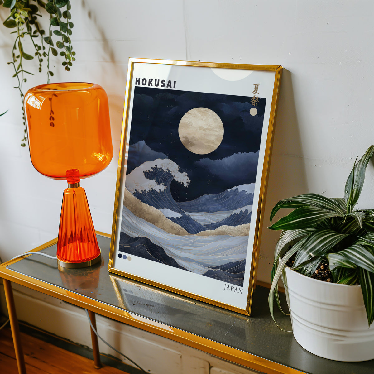 Hokusai night wave gold moon print shown in a gold frame on a console beside an orange glass lamp