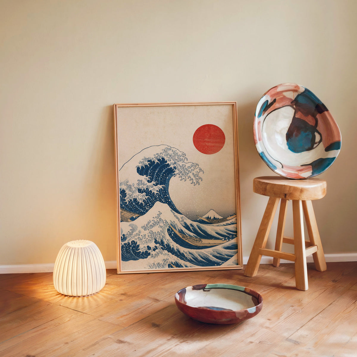 Great Wave with red sun print in a light wood frame leaning on a wooden floor by a glowing lamp and stool