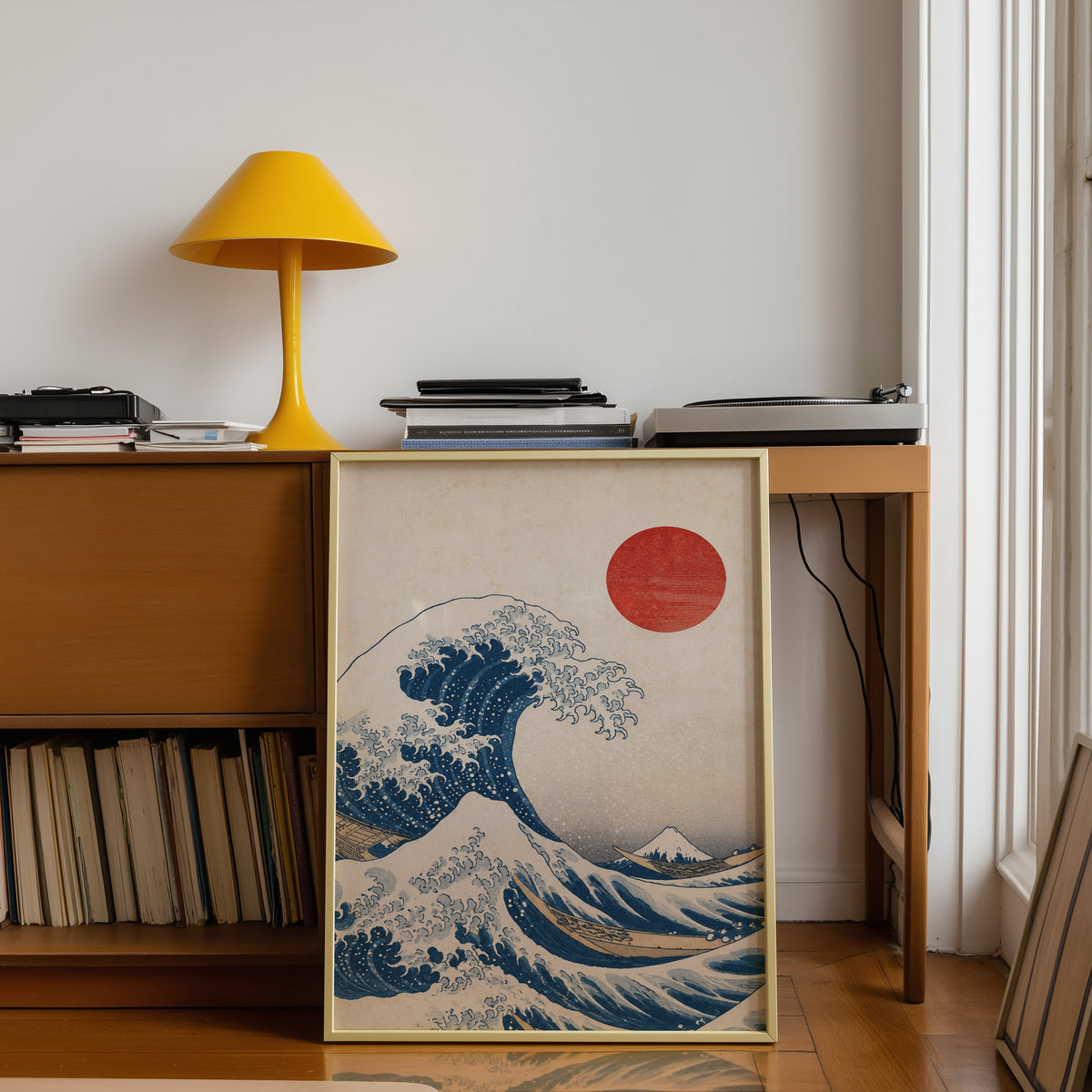 Great Wave with red sun print shown in a gold frame leaning under a teak desk with a yellow lamp
