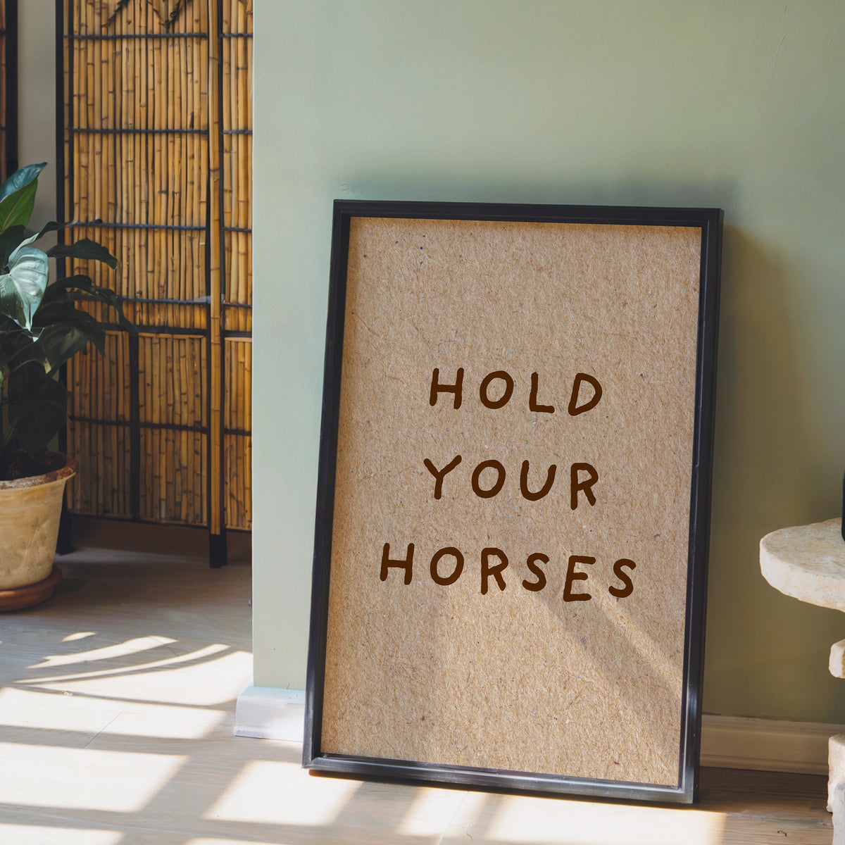 Hold Your Horses kraft print in a black frame leaning against a sage green wall