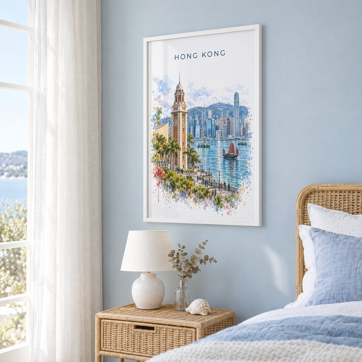 Hong Kong watercolor print in a white frame on a pale blue wall beside a rattan bed in a coastal bedroom