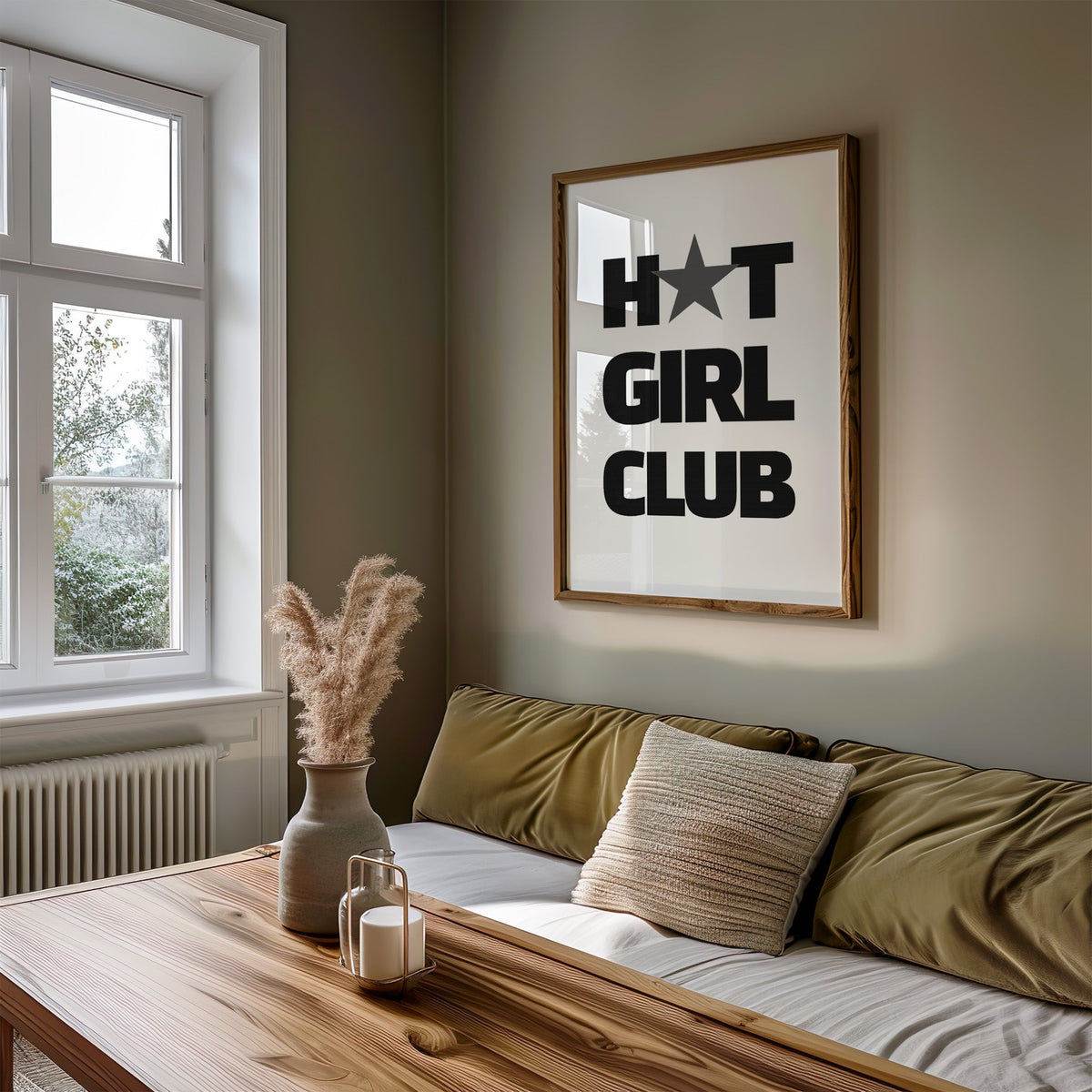 Bold Girl Club lettering with gray star print in a walnut frame above an olive daybed by a window