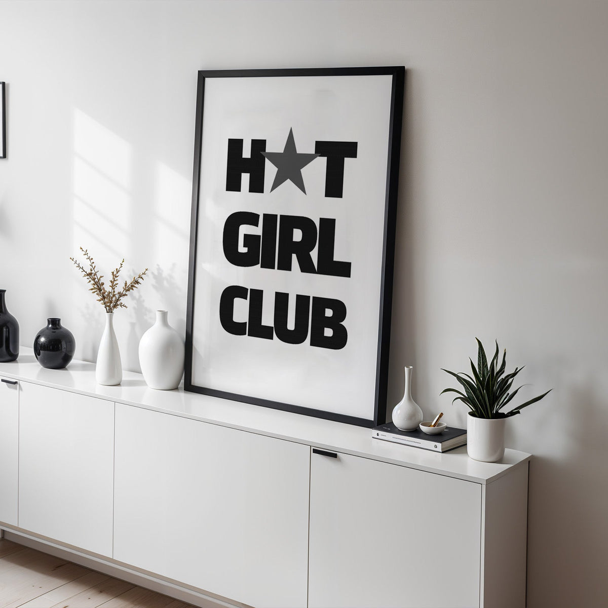 Bold Girl Club lettering with gray star print in a black frame on a white sideboard with black and white vases