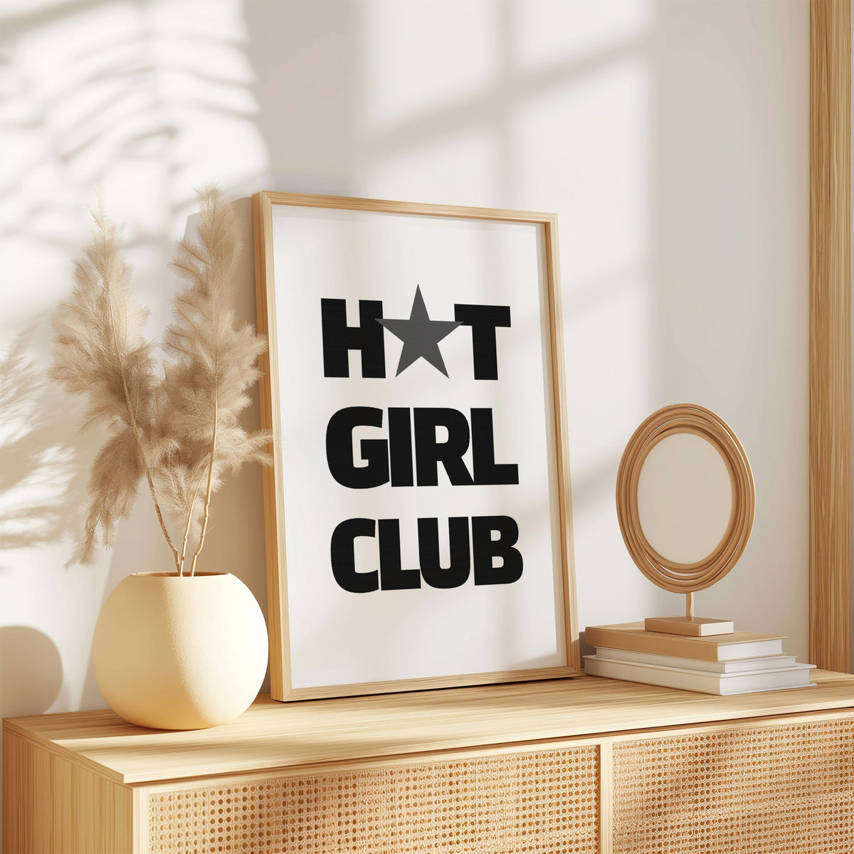 Bold Girl Club lettering with gray star print in an oak frame on a rattan sideboard beside pampas grass