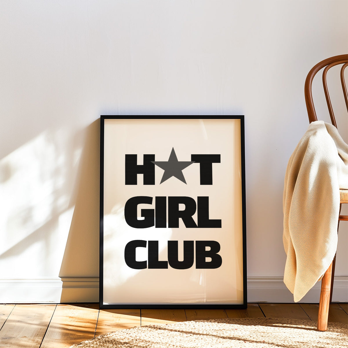 Bold Girl Club lettering with gray star print in a black frame leaning on a wood floor beside a bentwood chair