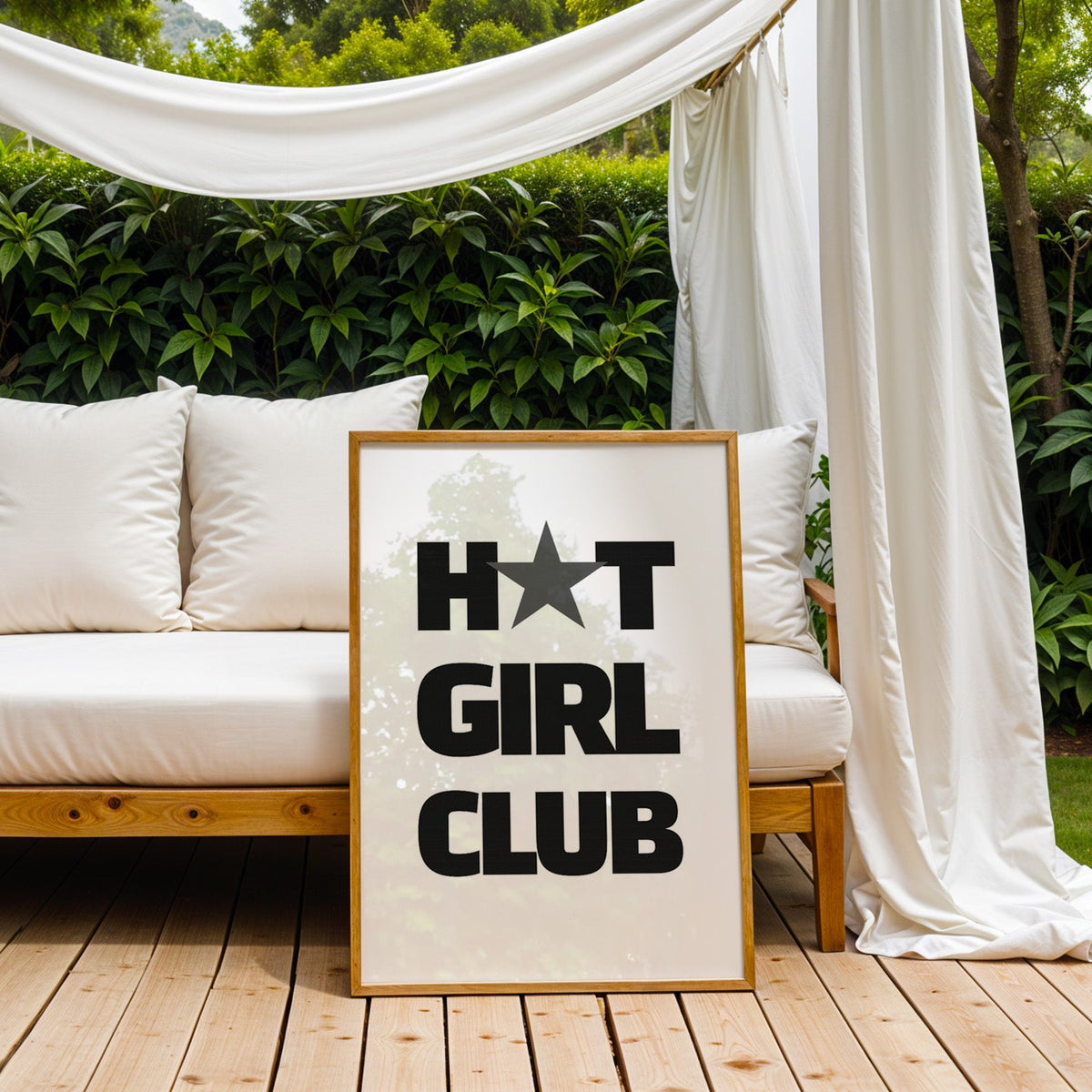 Bold Girl Club lettering with gray star print in an oak frame on an outdoor daybed under white drapes