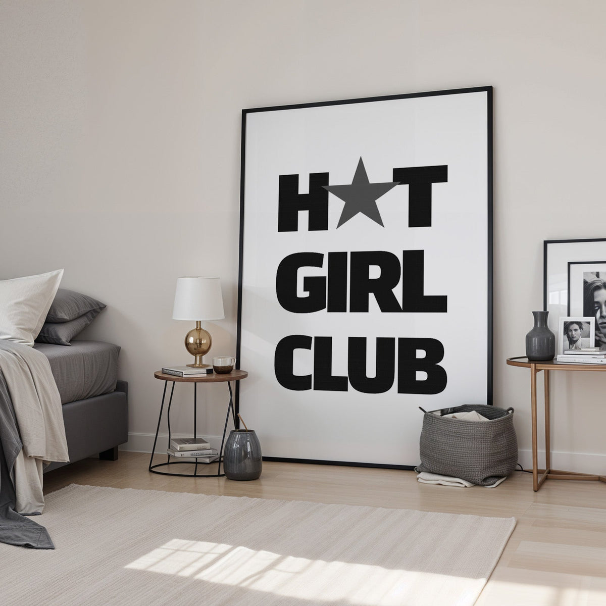 Bold Girl Club lettering with gray star print in a black frame leaning in a bedroom beside a gold lamp