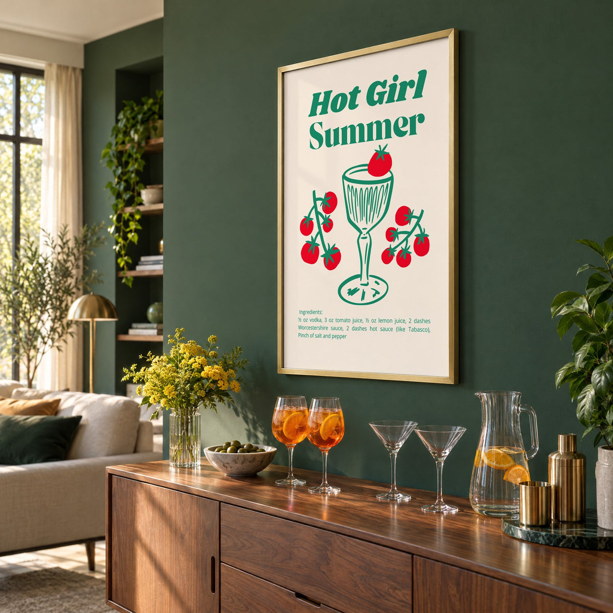 Hot Girl Summer tomato cocktail recipe print in a brass frame on a bottle green wall above a sideboard with spritz and martini glasses, seen at an angle