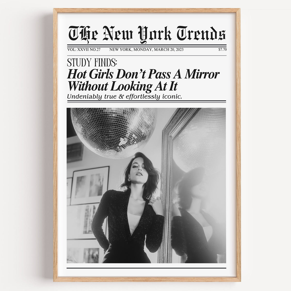 Woman by mirror with disco ball mock newspaper print in a light oak frame on a plain white wall