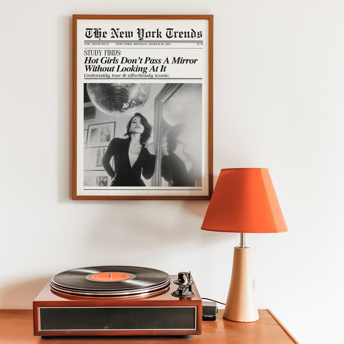 Woman by mirror with disco ball mock newspaper print in a walnut frame above a record player and orange lamp