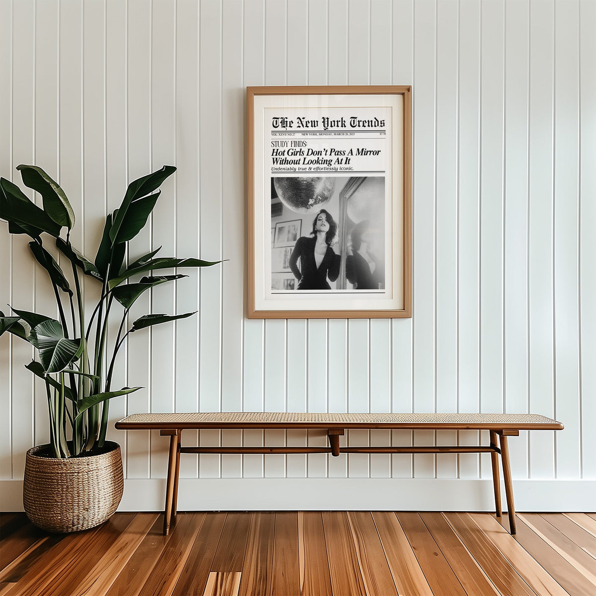 Woman by mirror with disco ball mock newspaper print in a wood frame with a white mat above a cane bench