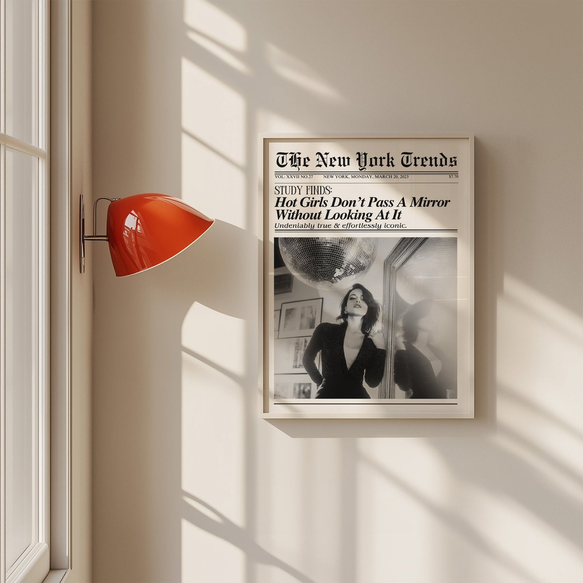 Woman by mirror with disco ball mock newspaper print in a white frame on a sunlit wall beside a red sconce