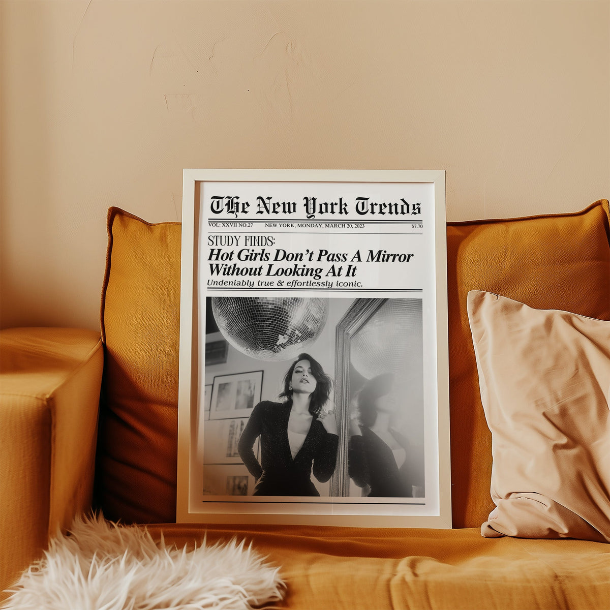 Woman by mirror with disco ball mock newspaper print in a white frame leaning on a mustard velvet sofa
