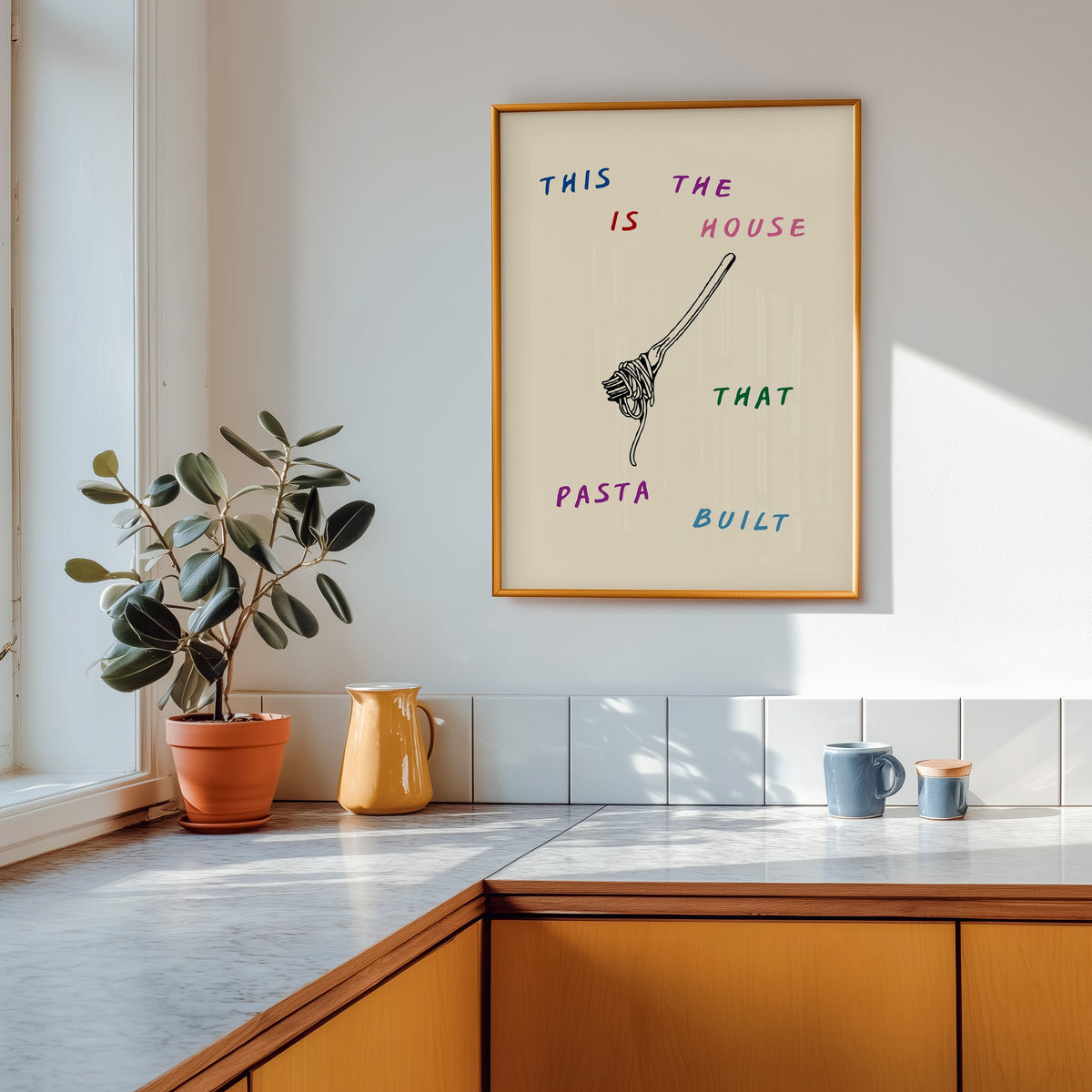 House That Pasta Built print in a gold frame above a marble counter with a yellow jug