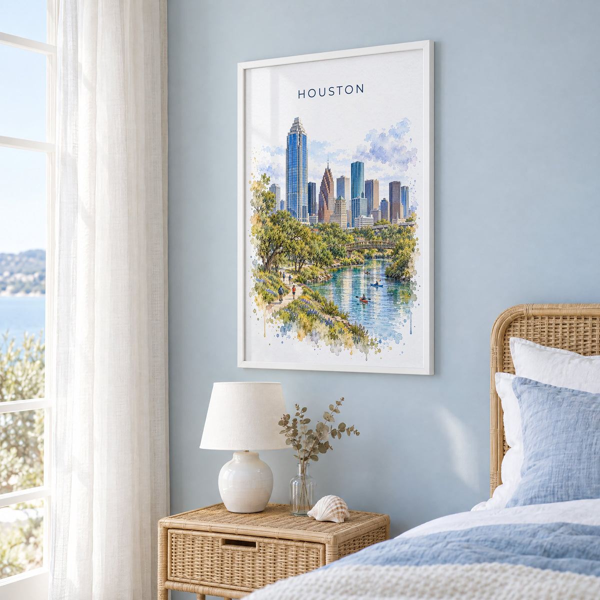 Houston watercolor print in a white frame on a pale blue wall beside a rattan bed in a coastal bedroom