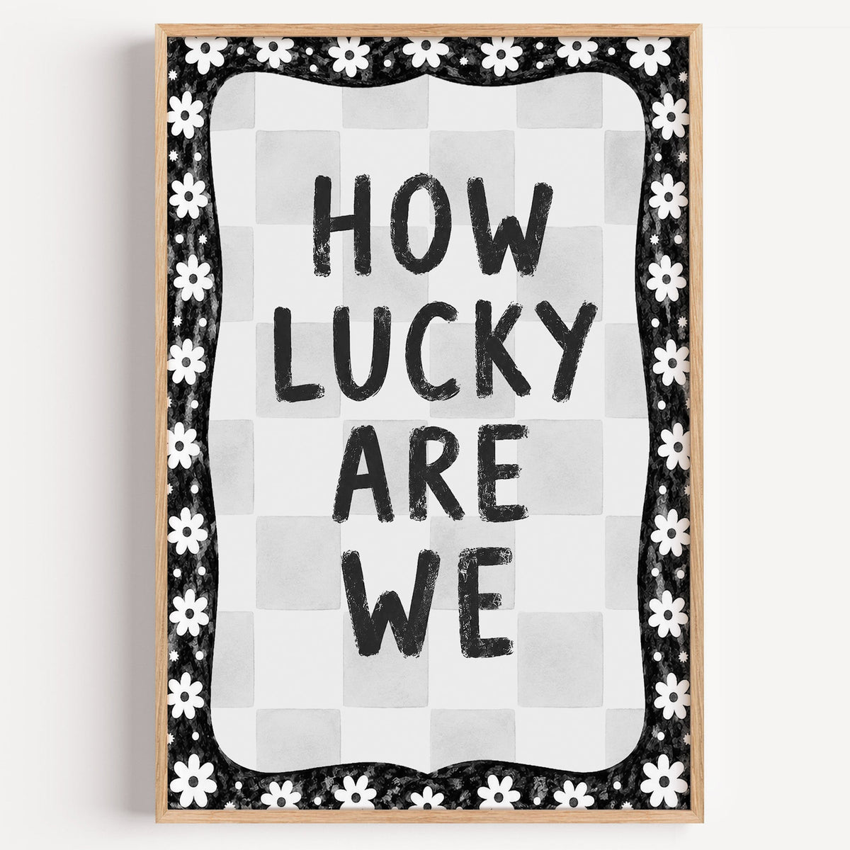How lucky are we quote with white daisy border print in a light oak frame on a plain white wall