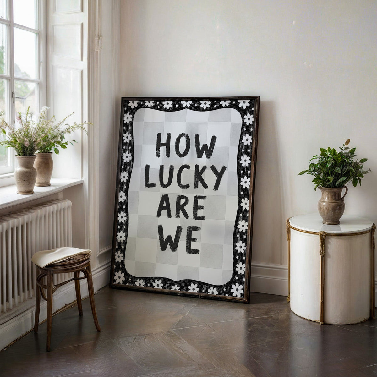 How lucky are we quote with white daisy border print in a black frame on a dark stone floor beside a white side table