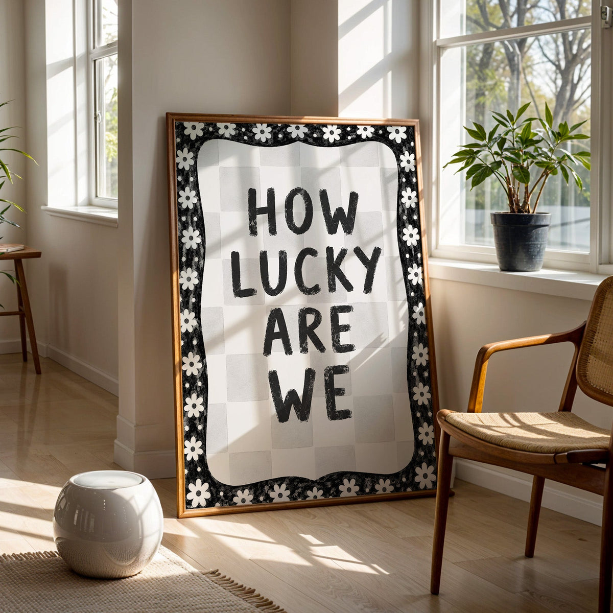 How lucky are we quote with white daisy border print in a walnut frame on a wood floor beside a cane chair and sunny window