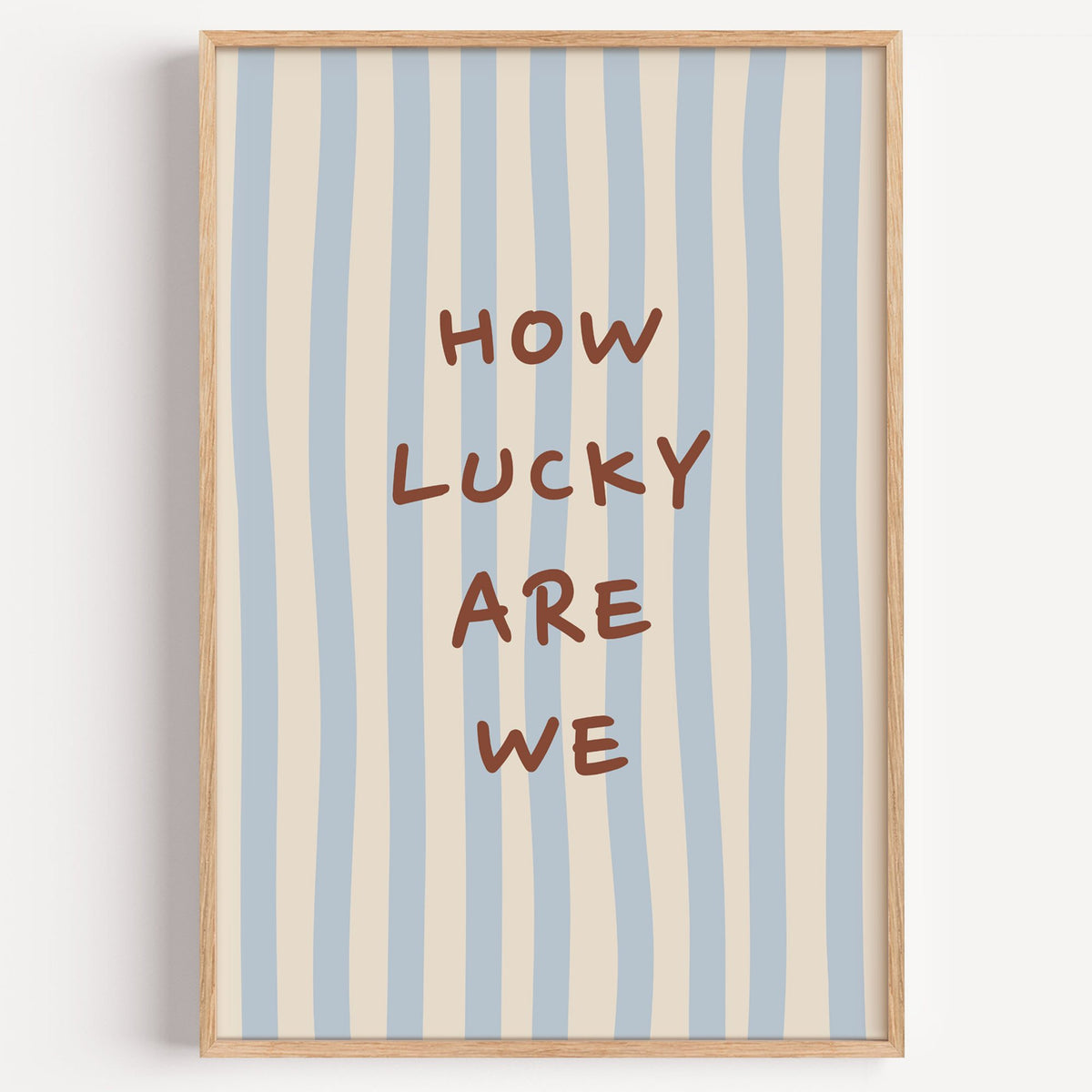 How lucky are we nursery print in a light oak frame on a plain white wall