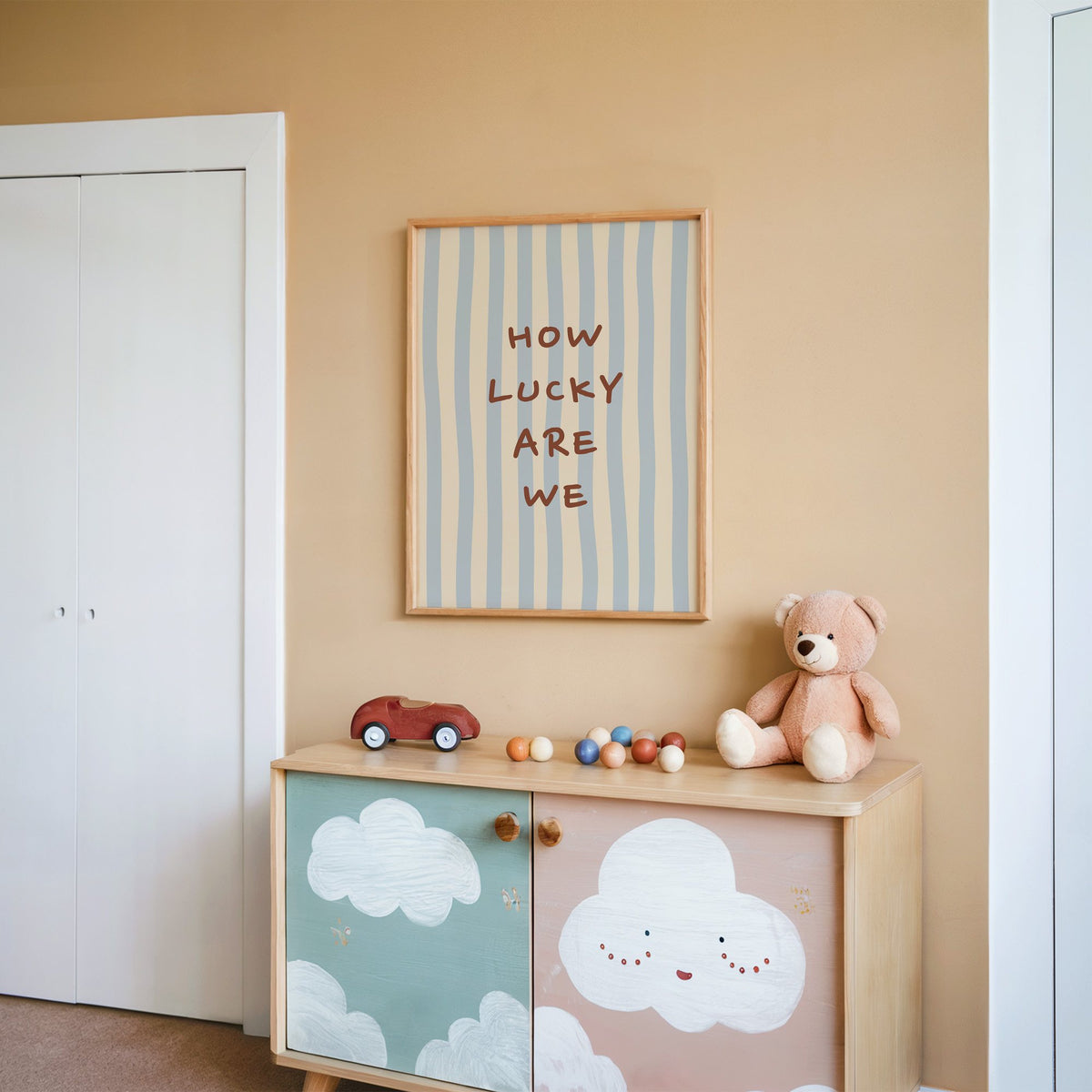 How lucky are we nursery print in an oak frame on a peach wall above a cloud-painted cabinet