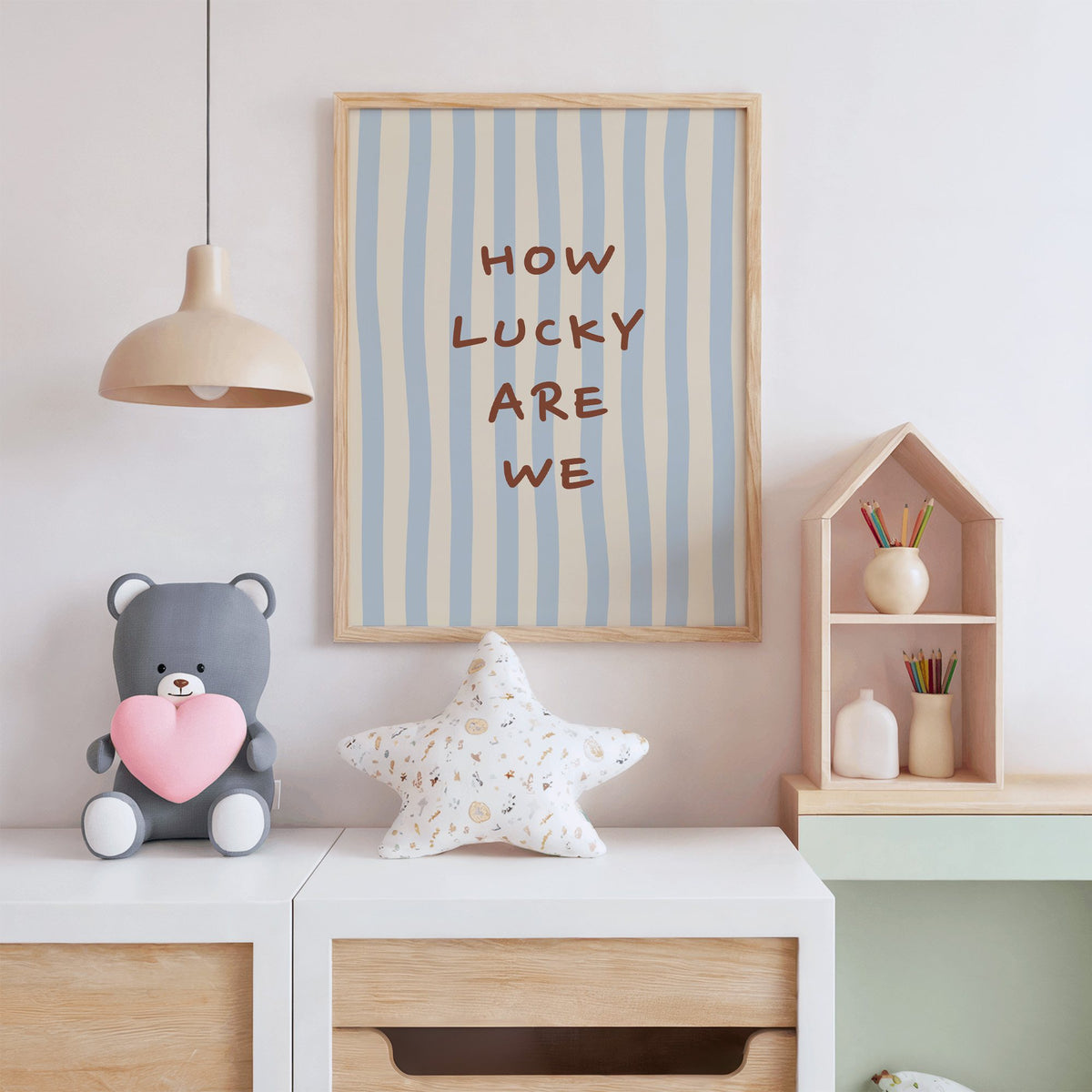 How lucky are we nursery print in an oak frame above a white dresser with a star pillow and house shelf