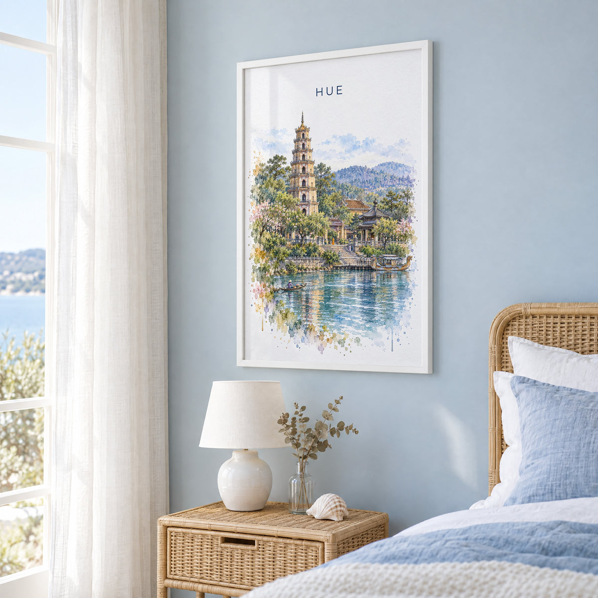 Hue, Vietnam watercolor print in a white frame on a pale blue wall beside a rattan bed in a coastal bedroom