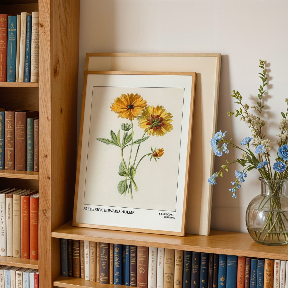 Coreopsis print in an oak frame leaning on a bookshelf beside blue flowers