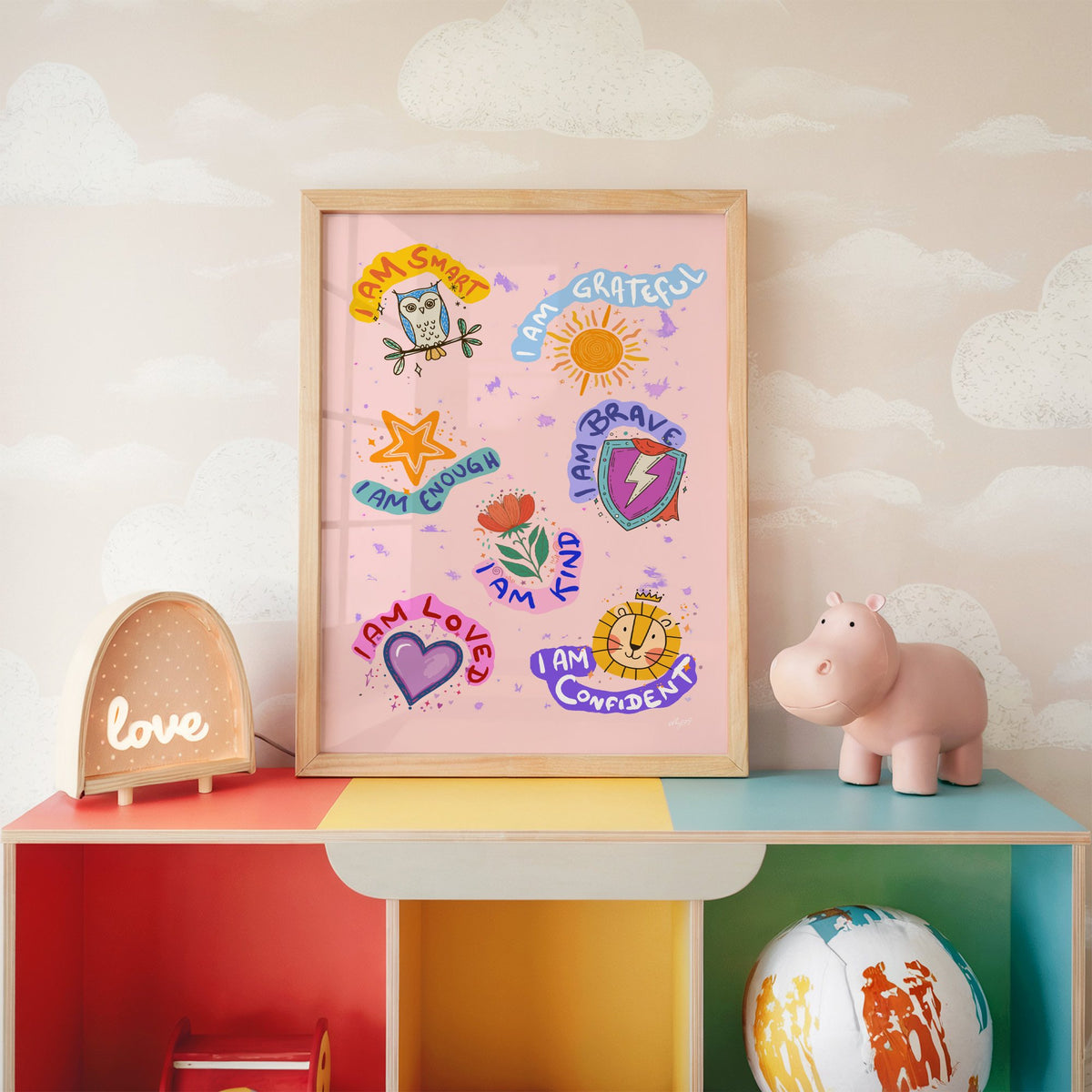 I am affirmations sticker nursery print in an oak frame on a rainbow toy shelf against cloud wallpaper