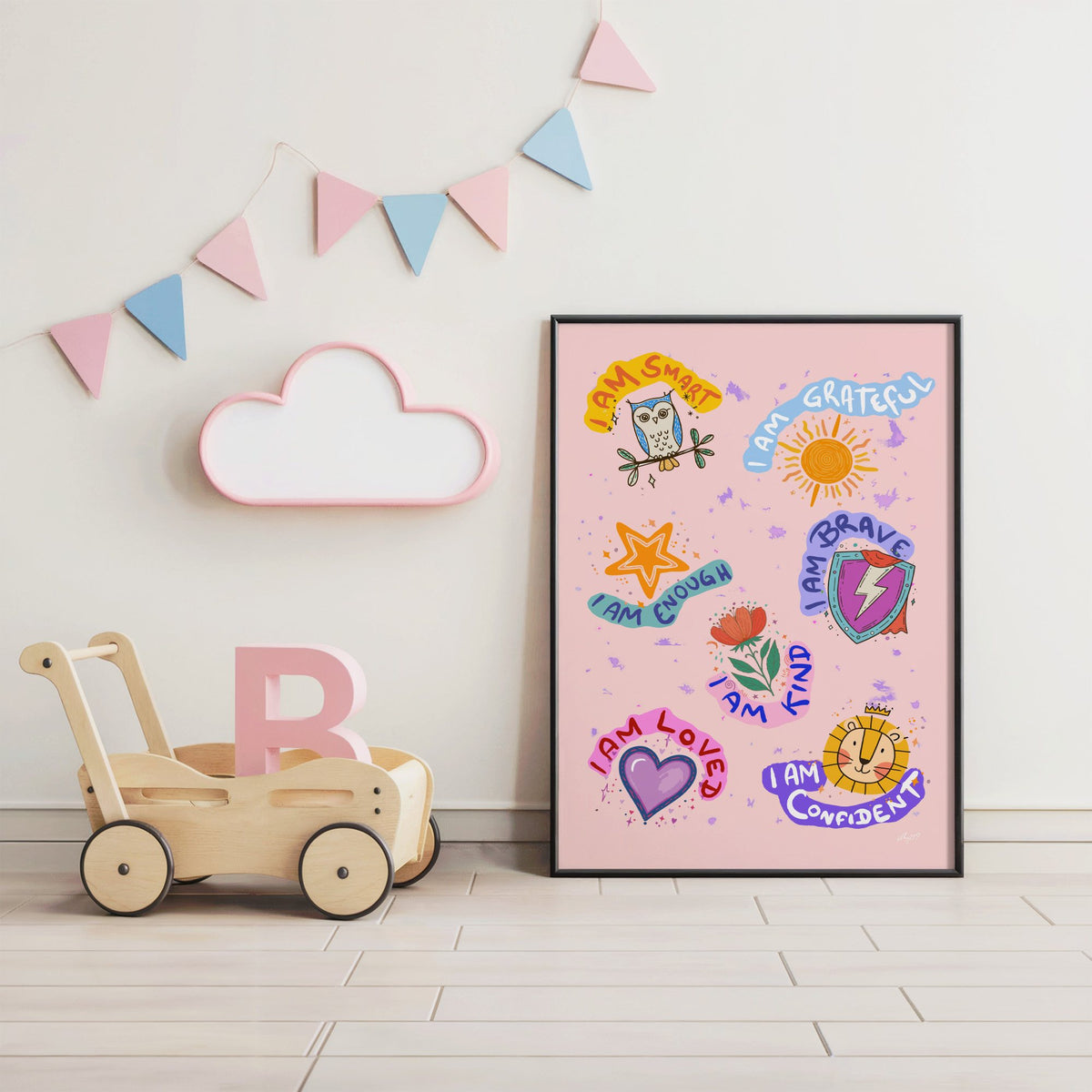 I am affirmations sticker nursery print in a black frame under pastel bunting by a wooden baby walker