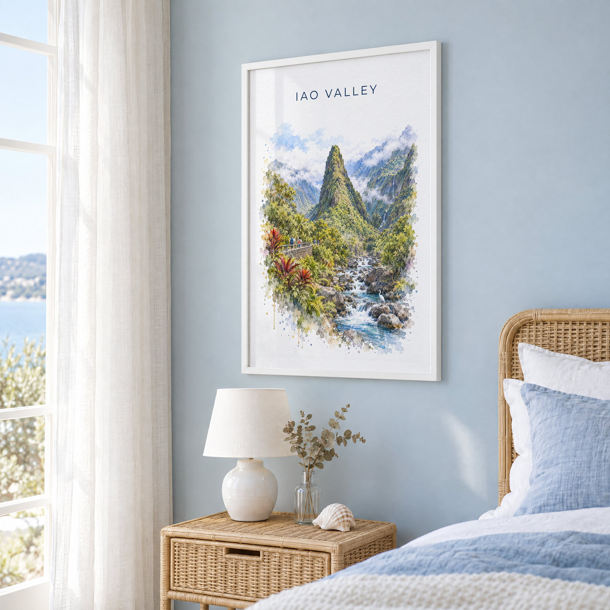 Iao Valley watercolor print in a white frame on a pale blue wall beside a rattan bed in a coastal bedroom