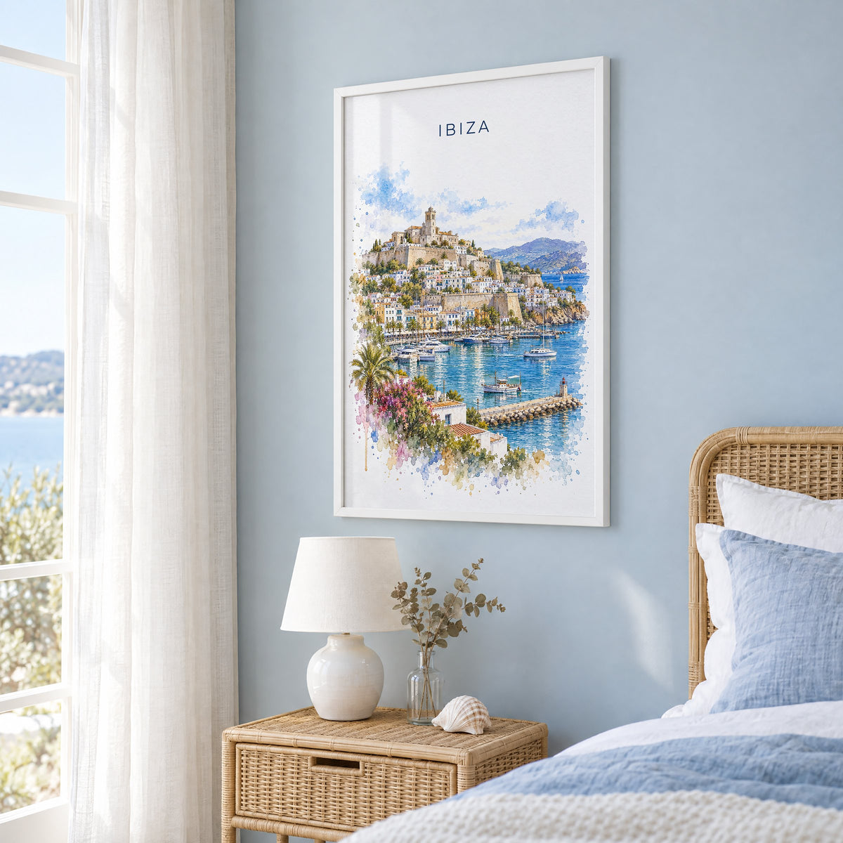 Ibiza watercolor print in a white frame on a pale blue wall beside a rattan bed in a coastal bedroom