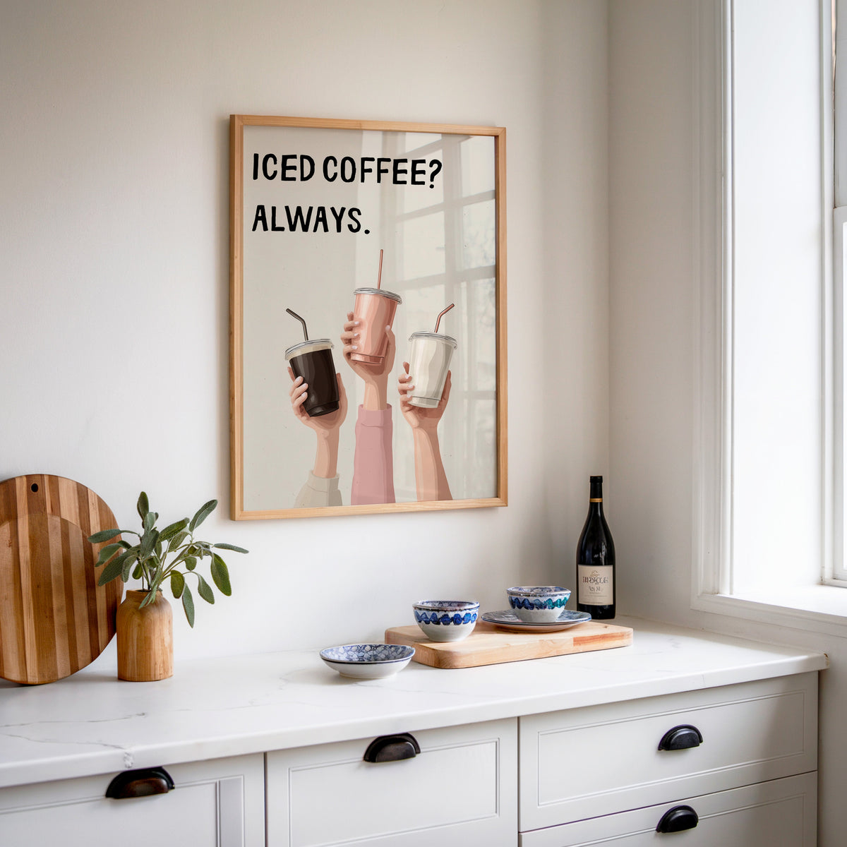 Iced Coffee Always print in an oak frame above a white sideboard with a bottle of wine