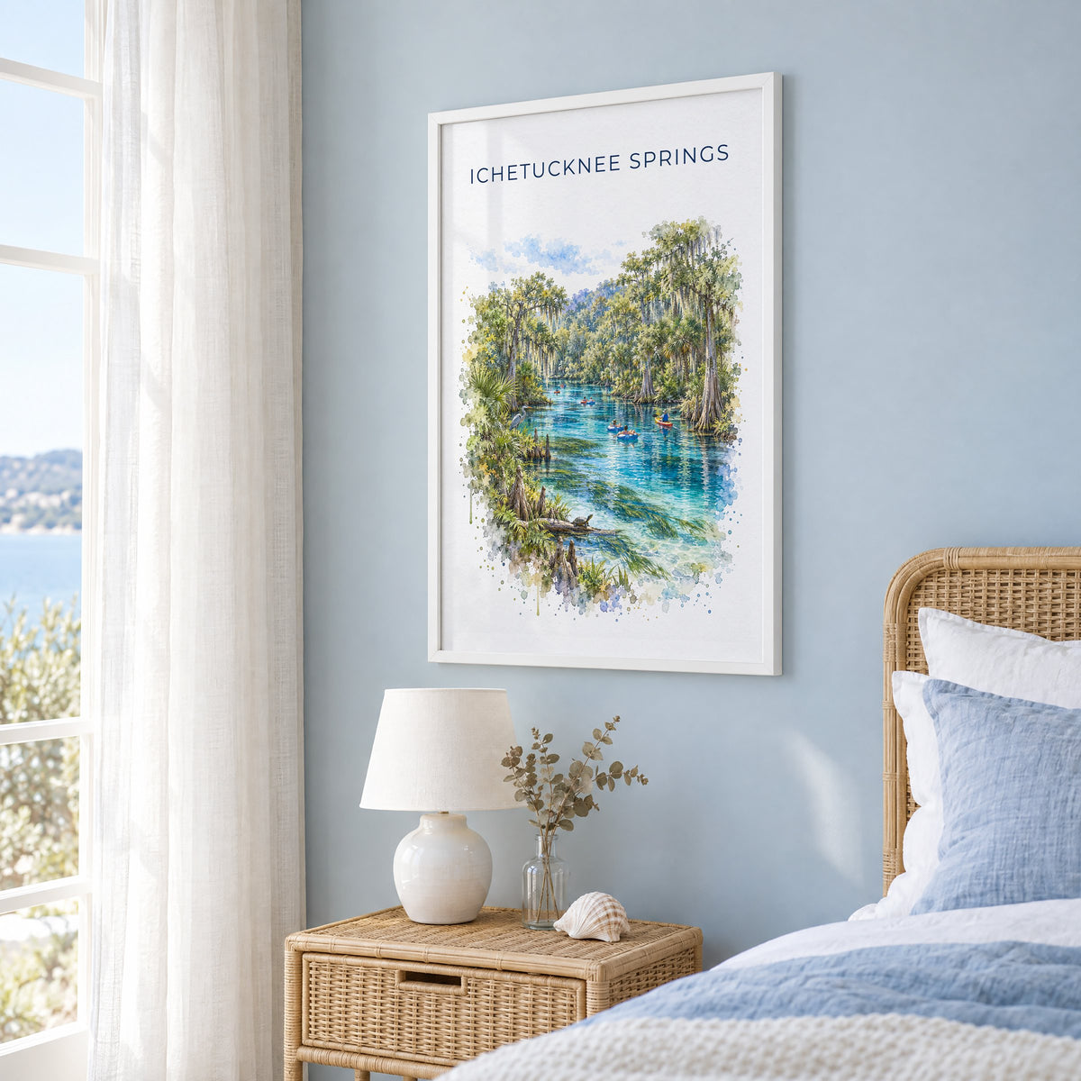 Ichetucknee Springs State Park watercolor print in a white frame on a pale blue wall beside a rattan bed in a coastal bedroom