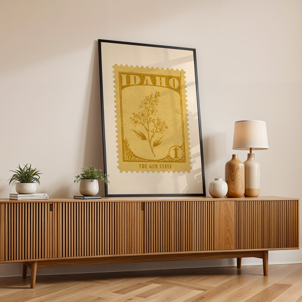 Idaho state flower print in a black frame leaning on a fluted wood credenza with vases and a lamp