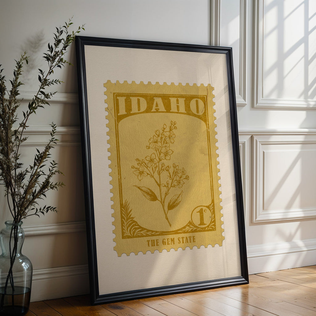 Idaho state flower print in a black frame leaning against a white panelled wall beside olive branches
