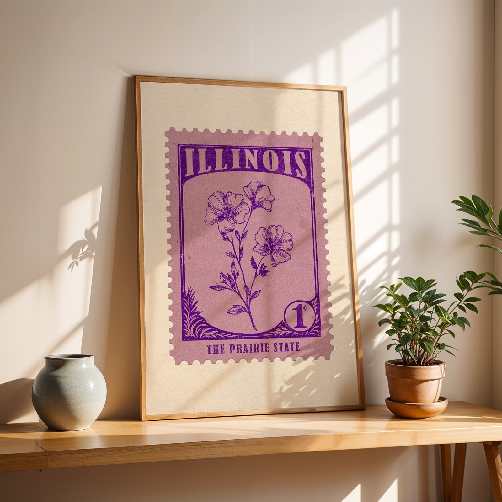Illinois violet stamp print in a light oak frame leaning on a wooden table beside a stoneware vase
