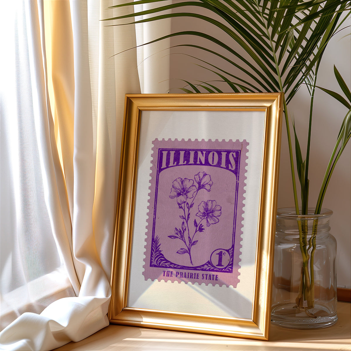 Illinois stamp print in a gold frame leaning by a cream curtain with a palm in a glass jar