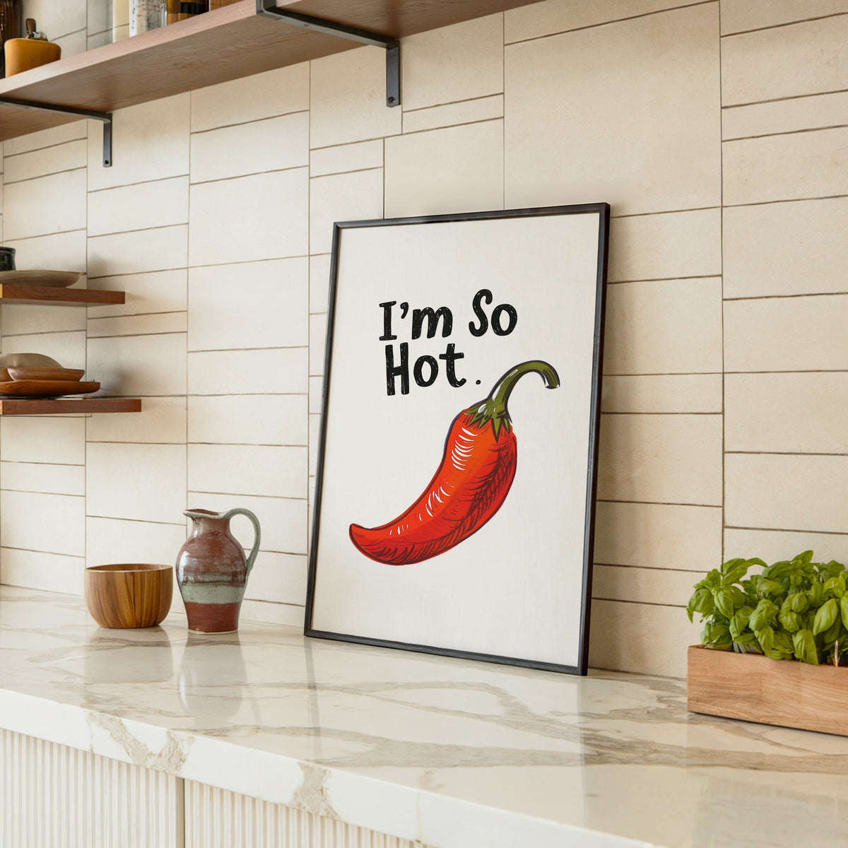 I'm So Hot chilli print in a black frame leaning on a marble counter in a tiled kitchen