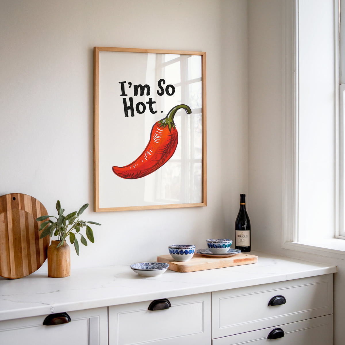 I'm So Hot chilli print in an oak frame above a white sideboard with a bottle of wine