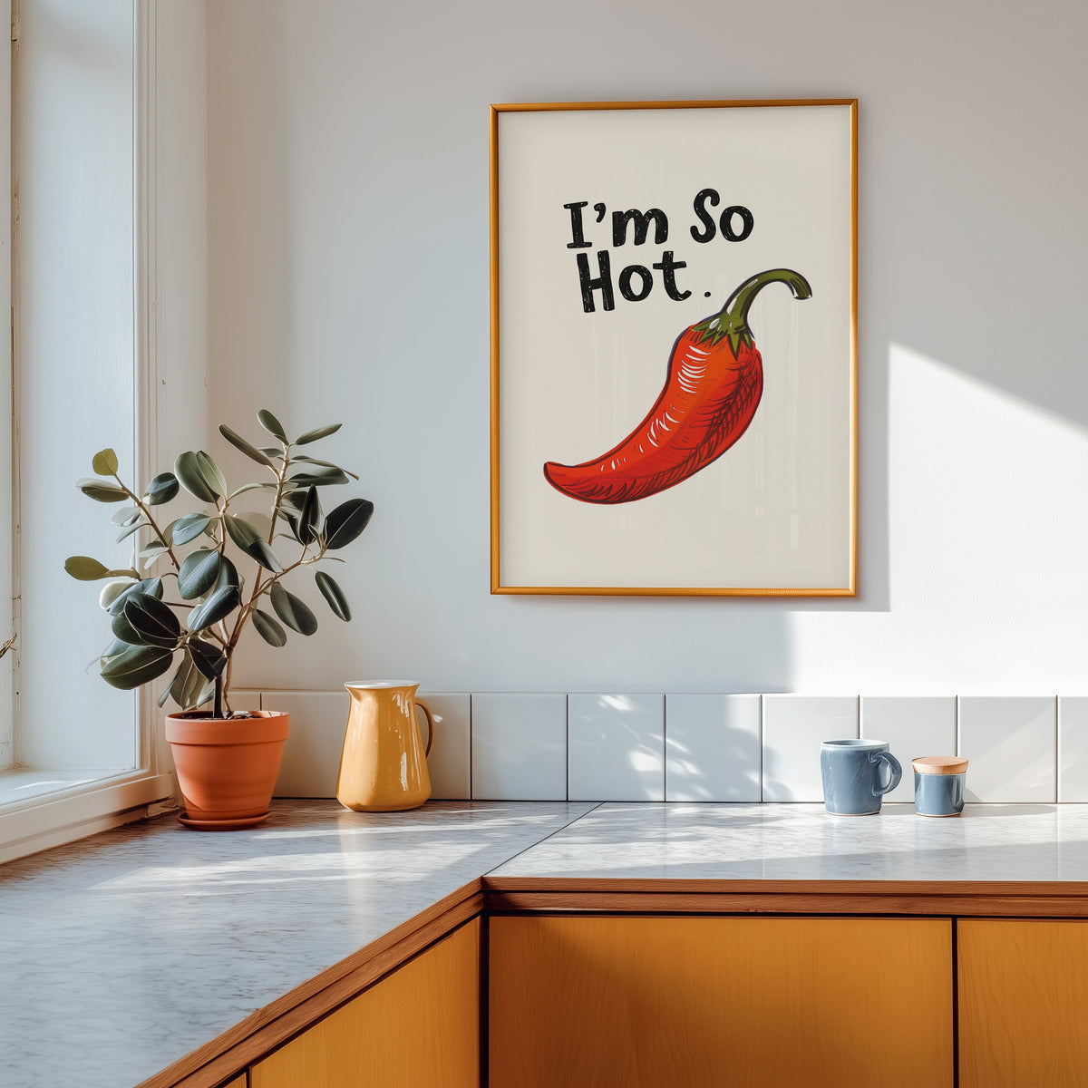 I'm So Hot chilli print shown in a gold frame above a marble counter in a tan kitchen