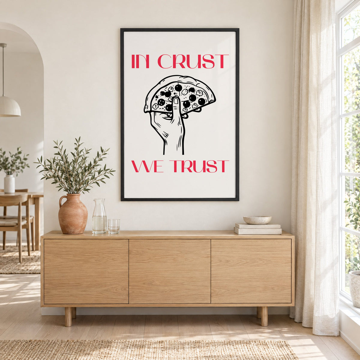 In Crust We Trust pizza print in a black frame above an oak sideboard with a terracotta vase of olive branches