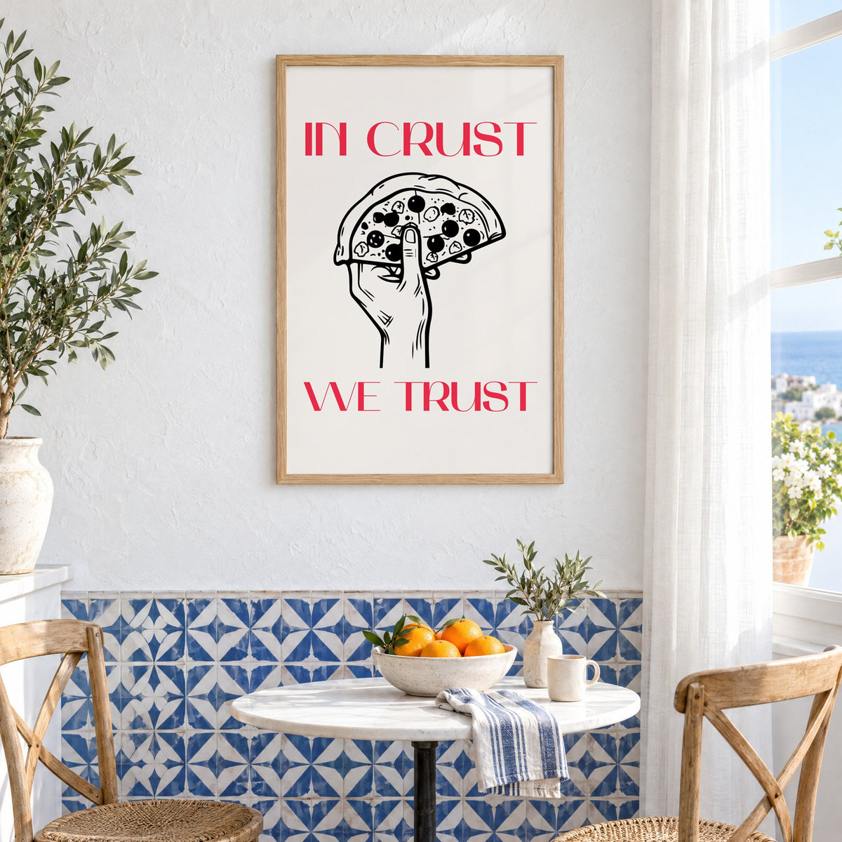 In Crust We Trust pizza print in an oak frame above a bistro table and blue patterned tiles