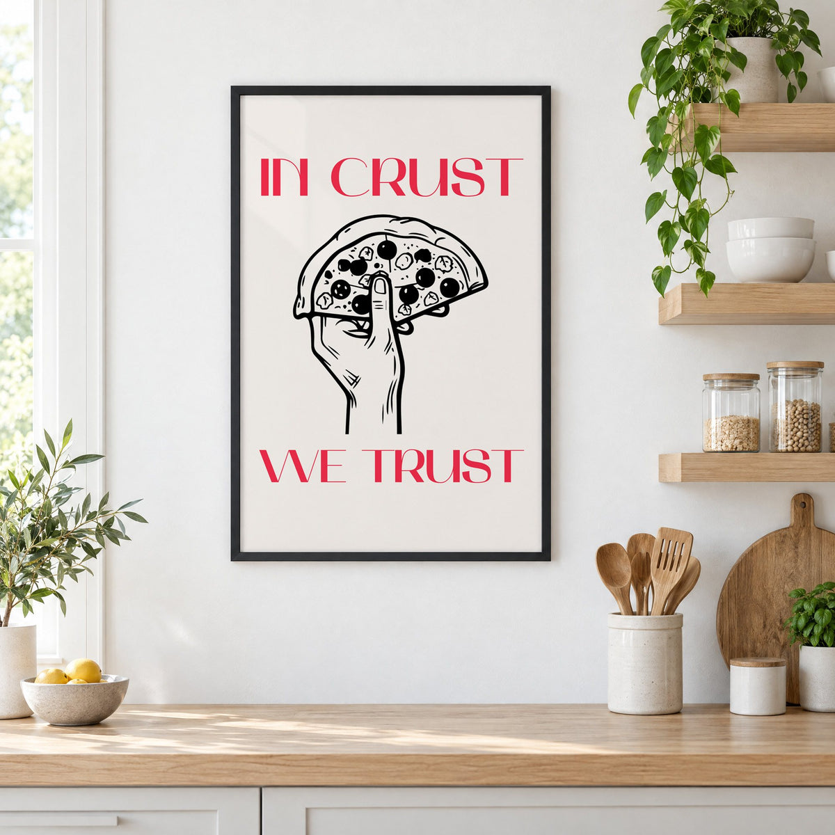 In Crust We Trust pizza print in a black frame in a white kitchen beside open wood shelves and glass jars