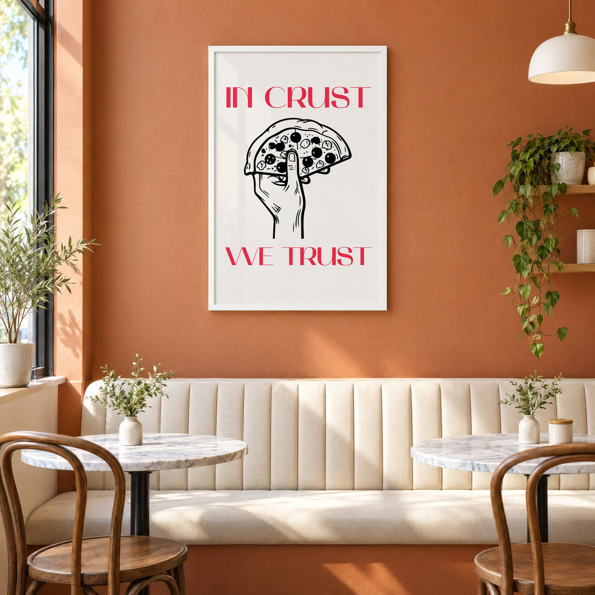 In Crust We Trust pizza print in a white frame above a cream banquette on a terracotta cafe wall