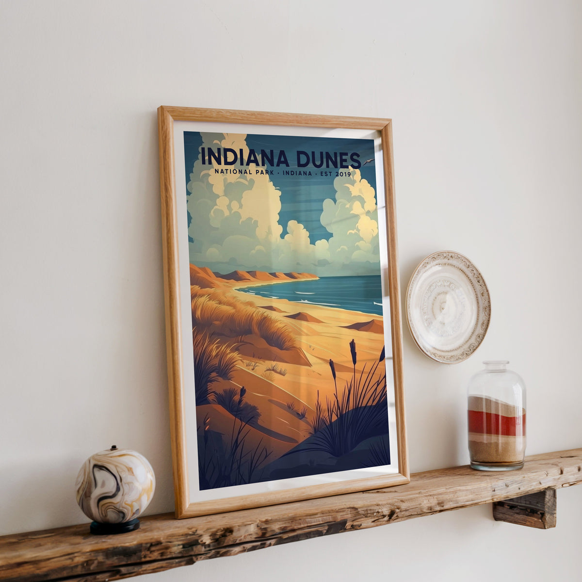 Indiana Dunes National Park print in an oak frame on a wood shelf with ceramics and a sand-filled jar