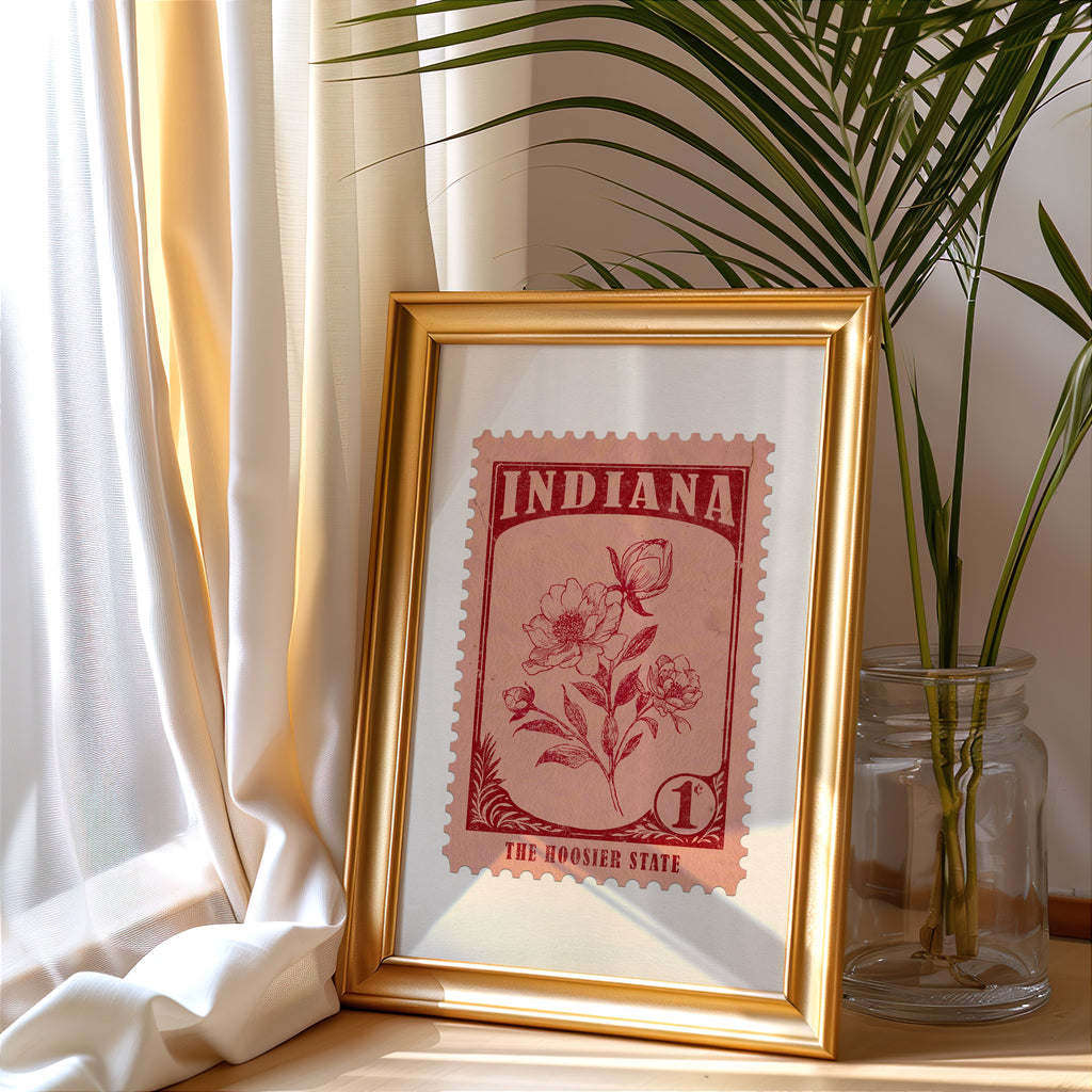 Indiana stamp print in a gold frame leaning by a cream curtain with a palm in a glass jar