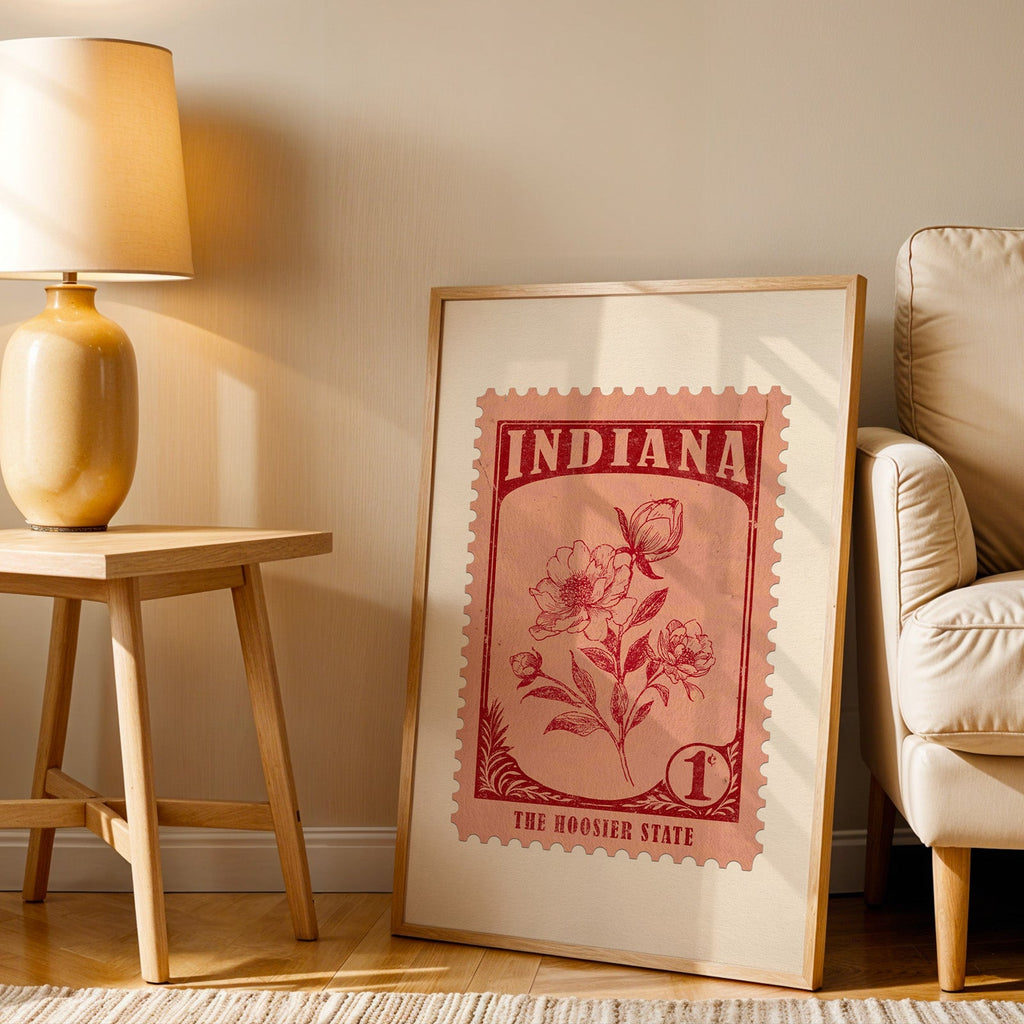 Indiana stamp print in a wood frame resting on the floor beside a beige armchair and a yellow lamp