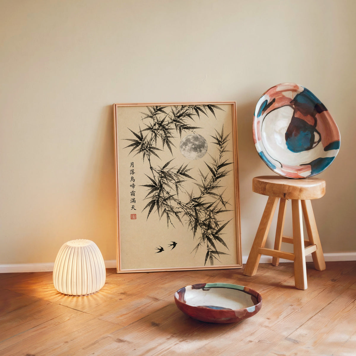 ink bamboo, full moon and swallows print in a light wood frame leaning on a wooden floor by a glowing lamp and stool