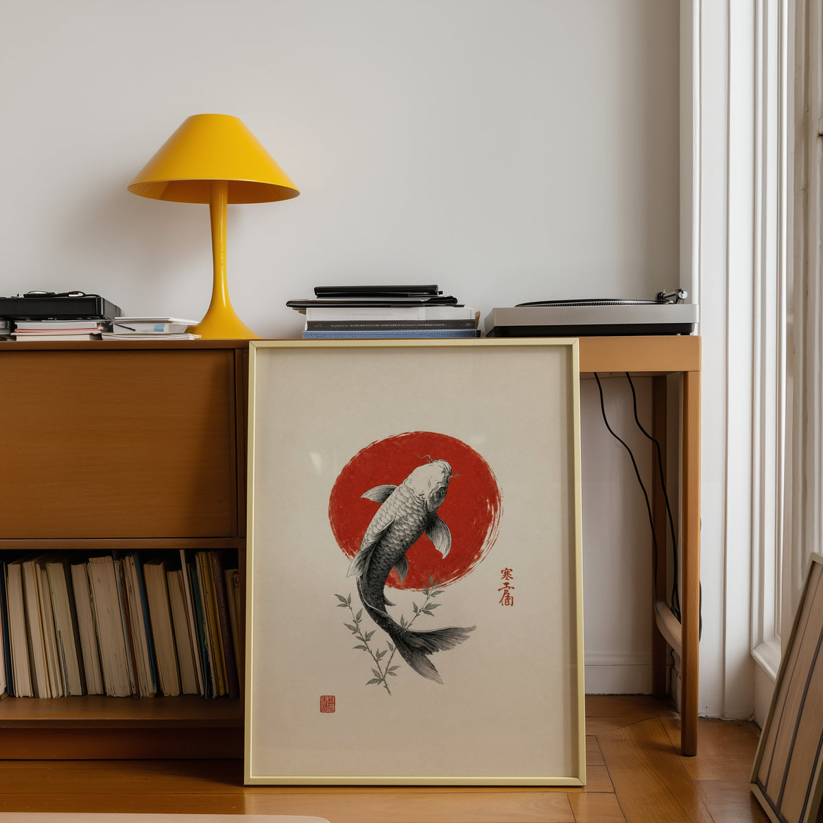 ink koi fish in red circle print shown in a gold frame leaning under a teak desk with a yellow lamp
